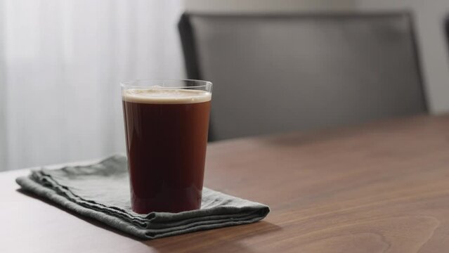 Slow motion nitro coffee in thin glass on walnut table