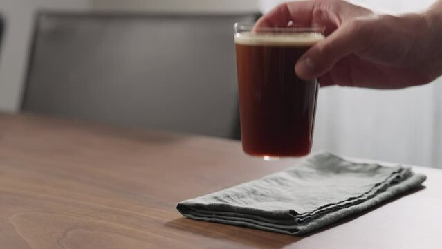 Slow motion man hand take nitro coffee in thin glass on walnut table
