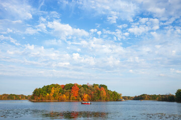 Father and son in fishing boat on a Minnesota lake with trees in fall color and beautiful clouds