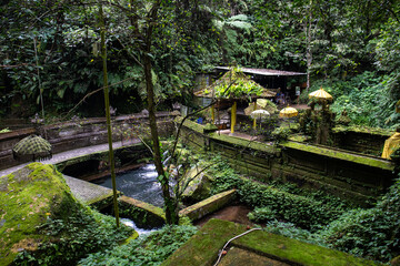 Fototapeta na wymiar A small temple used for holy ablutions. Haunted and covered in moss, with offerings, beautiful statues and because. Sacred springs and holy water in Bali, Indonesia