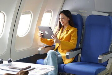 Asian woman sitting on airplane playing with cell phone and looking out window on vacation travel concept Talk about business on airplanes, listen to music, watch movies, relax, travel.