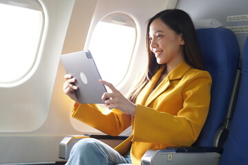 Asian woman sitting on airplane playing with cell phone and looking out window on vacation travel concept Talk about business on airplanes, listen to music, watch movies, relax, travel.