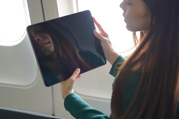 Asian woman sitting on airplane playing with cell phone and looking out window on vacation travel concept Talk about business on airplanes, listen to music, watch movies, relax, travel.