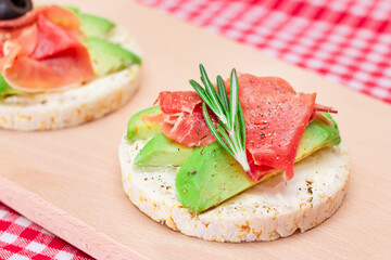Rice Cake Sandwich with Avocado, Jamon, Olives and Rosemary on Wooden Cutting Board. Easy...