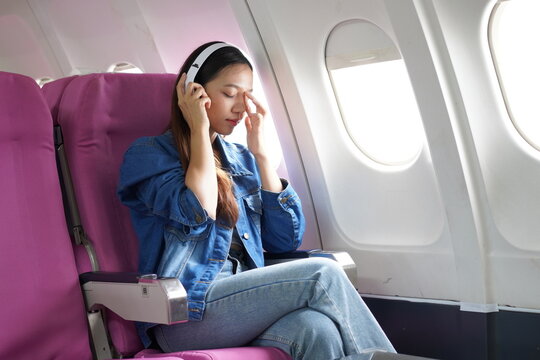 Asian woman sitting on airplane playing with cell phone and looking out window on vacation travel concept Talk about business on airplanes, listen to music, watch movies, relax, travel.