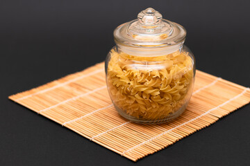 Uncooked Fusilli Pasta in Glass Jar on Black Background. Raw and Dry Macaroni. Unhealthy and Fat...