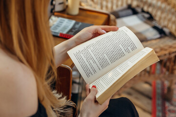 female hands holding a vintage book. girl reading a book sitting on a straw chair