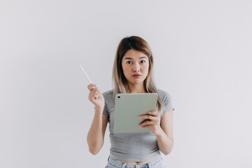 Asian Thai woman wear grey, hands holding tablet and white pen, have no idea suspicious, doubt face while working and looking at the camera, isolated on white background.