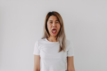 Asian Thai woman wear grey, standing isolated over white background, funny ugly sad face, feeling...