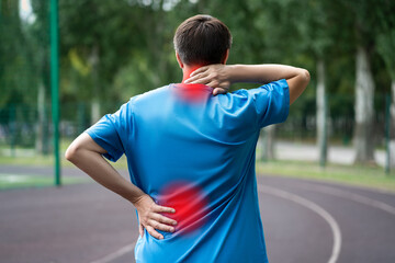 Back pain, athletic man with backache on a running track after workout