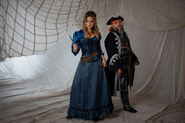 A lady and a pirate in an antique doublet and hat, a couple in pirate costumes. sails on the background - 665722583