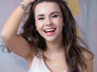 Sequins in makeup, a fashionable youth trend. Beautiful young girl happy and laughing, portrait in the Studio. makes a mustache by the hair - 665727907