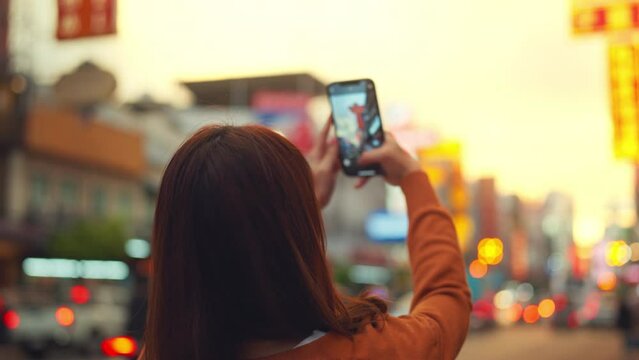 Happy young Asian tourist woman taking photo by mobile smartphone, Female traveller taking photo of Chinatown street food market during sunset in Bangkok, Thailand, Summer journey trip concept.