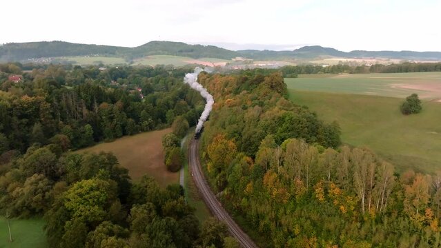 Aerial view of an autumn landscape with a passing historical steam train among the colorful leaves of trees. Czech countryside landscape