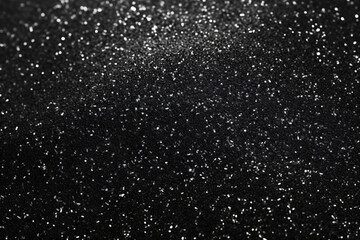 Black glitter texture made up of small particles unevenly distributed.