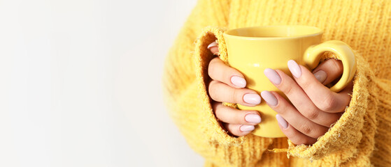 Young woman with stylish manicure holding cup on light background with space for text, closeup