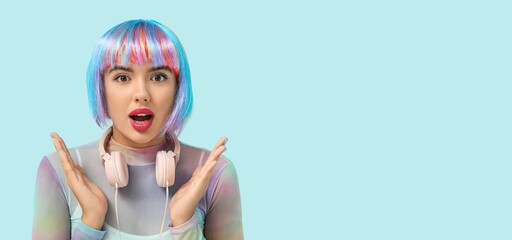 Portrait of shocked young woman in colorful wig and with headphones on light blue background with space for text