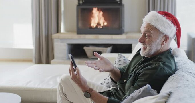 Middle aged caucasian man in santa hat using smartphone at christmas at home, slow motion
