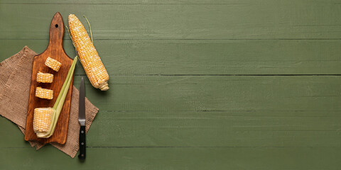 Board and fresh corn cobs on green wooden background with space for text