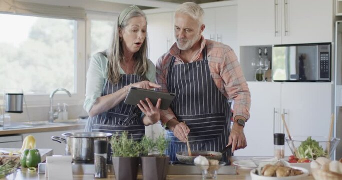 Middle aged caucasian couple with tablet, preparing meal, cooking in kitchen at home, slow motion