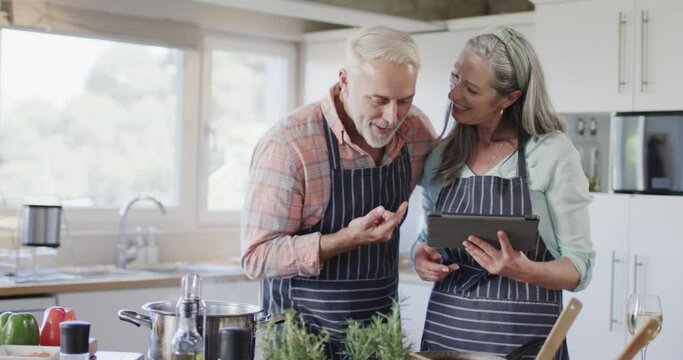 Middle aged caucasian couple using tablet, preparing meal, cooking in kitchen at home, slow motion