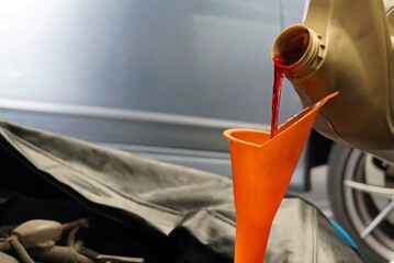 Car mechanic pouring gear oil into a motor oil canister in a car repair shop.