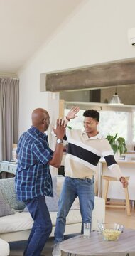 Vertical video of african american father and son cheering sport on tv and high fiving, slow motion