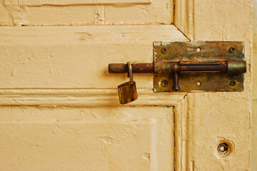 old metal lock latch on yellow dirty  door with padlock