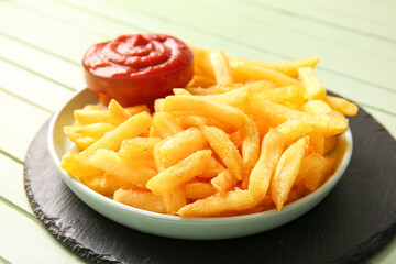Plate with tasty french fries and bowl of ketchup on color wooden background, closeup