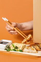 Female hand with chopsticks, Chinese dumplings, tofu cheese and soy sauce on color background, closeup