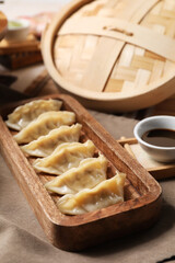 Wooden board with tasty Chinese dumplings and soy sauce on table, closeup