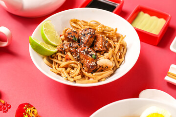 Bowl with tasty Chinese noodles with chicken and sauces on red background