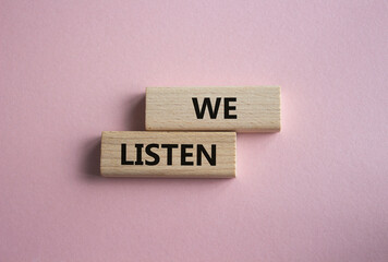 We listen symbol. Wooden blocks with words We listen. Beautiful pink background. Business and We listen concept. Copy space.