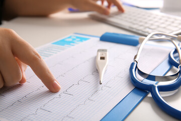 Female doctor working with cardiogram on white medical desk, closeup