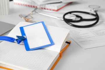 Blank badge with notebook on white medical desk, closeup