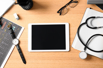 Blank tablet computer with accessories on wooden medical desk, top view