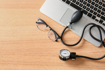 Sphygmomanometer with laptop and eyeglasses on wooden medical desk, closeup