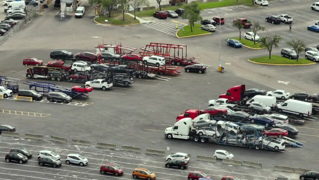 Big rig long haul semi truck tractors transporting used cars on two level modular semi trailers at auction dealer company big parking lot. Sales of secondhand vehicles