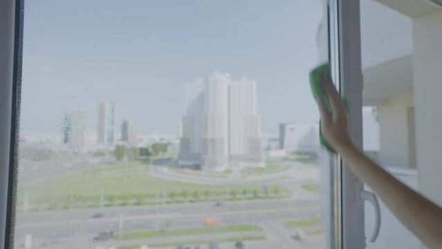 Female hand with soft sponge washes glass of window with splashes of detergent on surface. Home cleaning and service