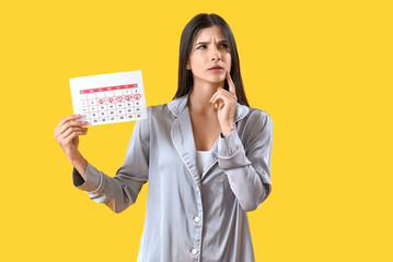 Thoughtful young woman with menstrual calendar on yellow background