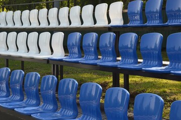 Blue and white empty plastic seats on the stands of a sports stadium on a summer day.