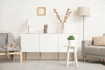 Obraz premium Interior of light living room with grey sofa, armchair and white sideboard