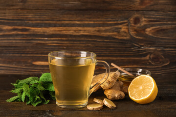 Glass cup of ginger tea with lemon and mint on wooden background