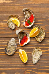 Tasty oysters with lemon and red caviar on wooden background