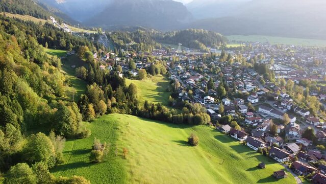 Ortsansicht von Oberstdorf umrahmt von Wiesen und den Allgäuer Alpen bei Abendlicht, Luftaufnahme