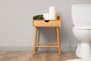 Wooden table with paper rolls and houseplant near toiled bowl in modern restroom, closeup