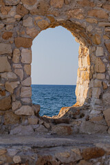 Rock wall with a window hole to the blue quiet Mediterranean Sea, in Chania, Crete, Greek Islands