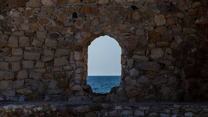 Rock wall with a window hole to the blue quiet Mediterranean Sea, in Chania, Crete, Greek Islands