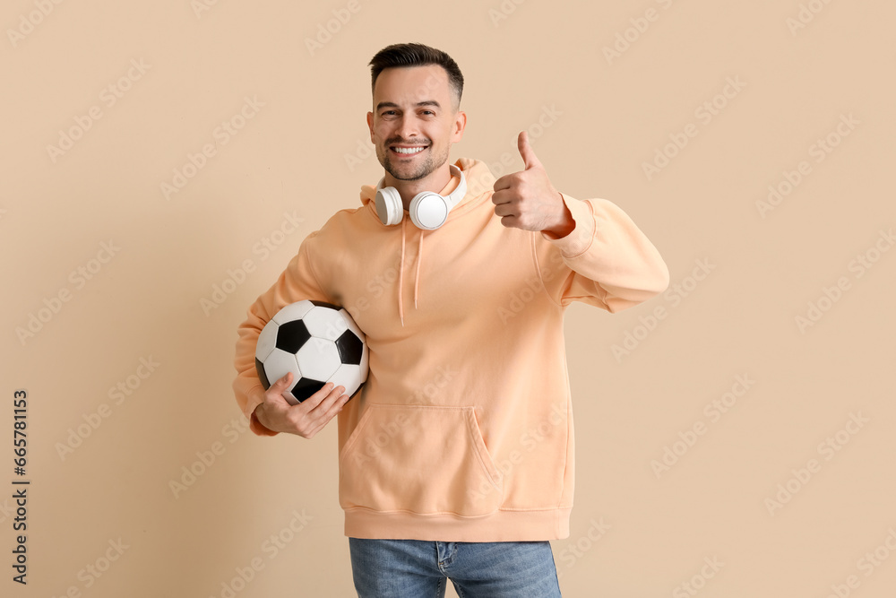 Poster happy young man with soccer ball showing thumb-up on beige background