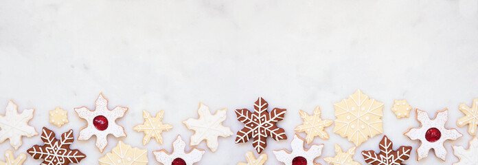 Christmas baking bottom border with a variety of snowflake cookies. Top view on a white marble background with copy space. Holiday baking concept.